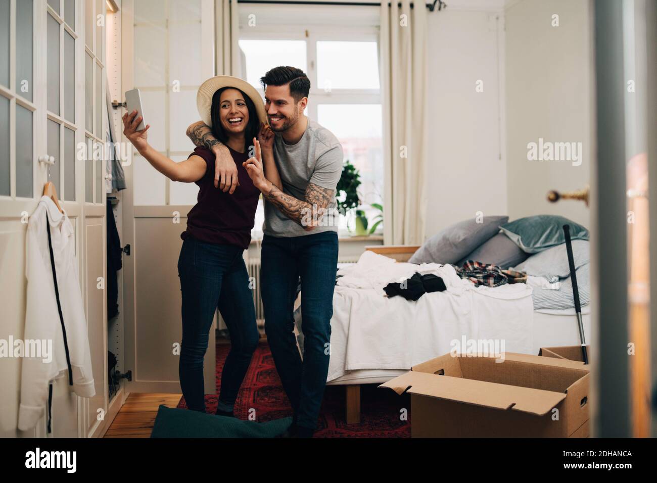 Lächelndes Paar, das Selfie auf dem Handy nimmt, während es im Stehen ist Schlafzimmer Stockfoto