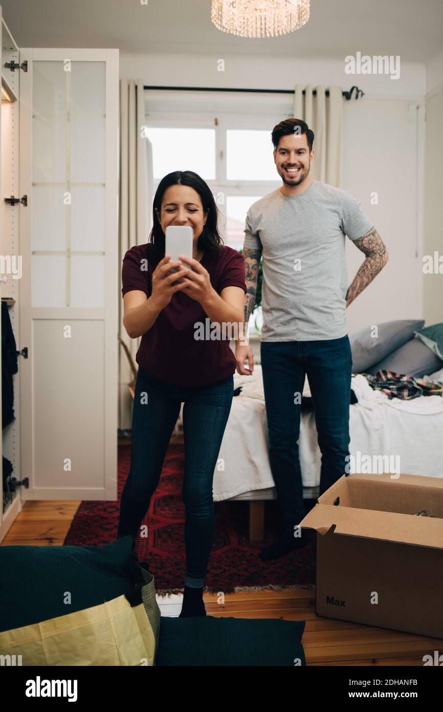 Frau, die Selfie auf dem Handy nimmt, während sie mit dem Mann steht Im Schlafzimmer Stockfoto