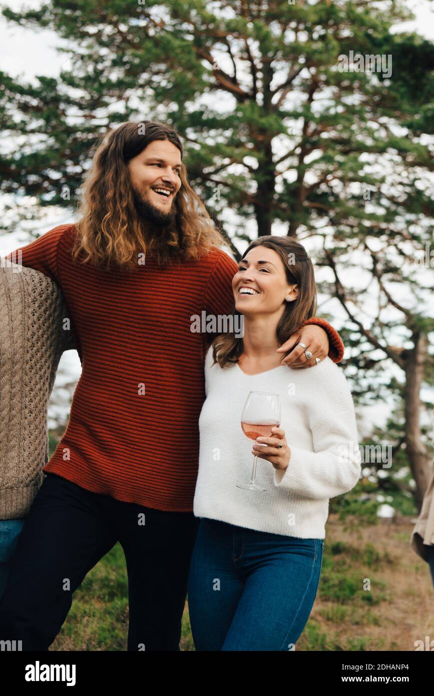 Glückliche Frau mit Wein, während Sie mit einem lächelnden Freund im Freien spazieren Stockfoto