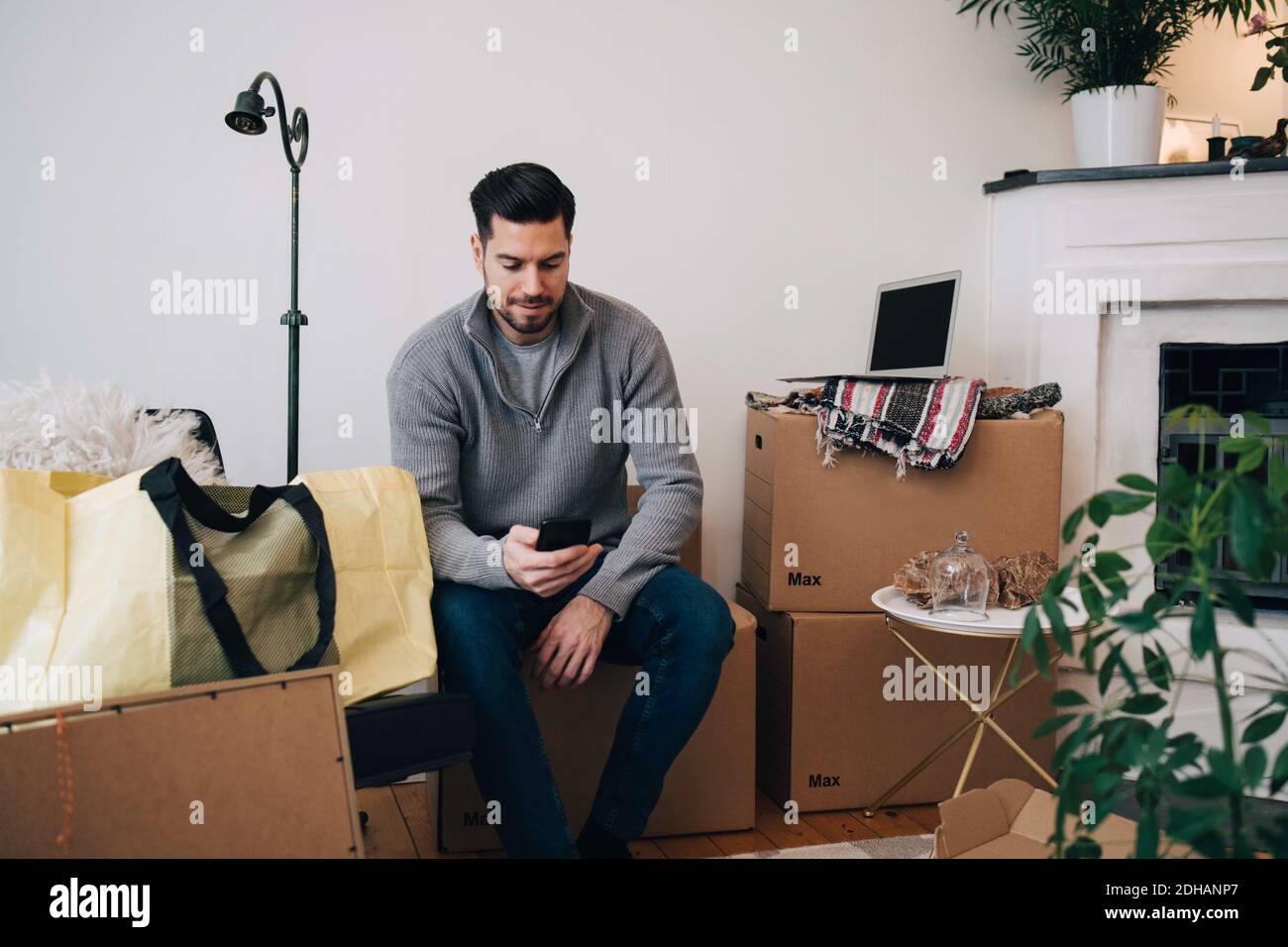 Mann mit mittlerem Erwachsenen, der Mobiltelefon benutzt, während er auf der Box sitzt Zu Hause Stockfoto