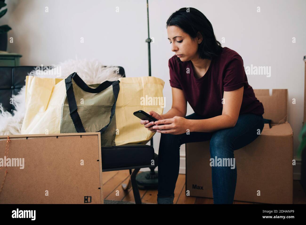 Mittlere Erwachsene Frau mit Mobiltelefon, während sie auf der Box sitzt Gegen die Wand Stockfoto