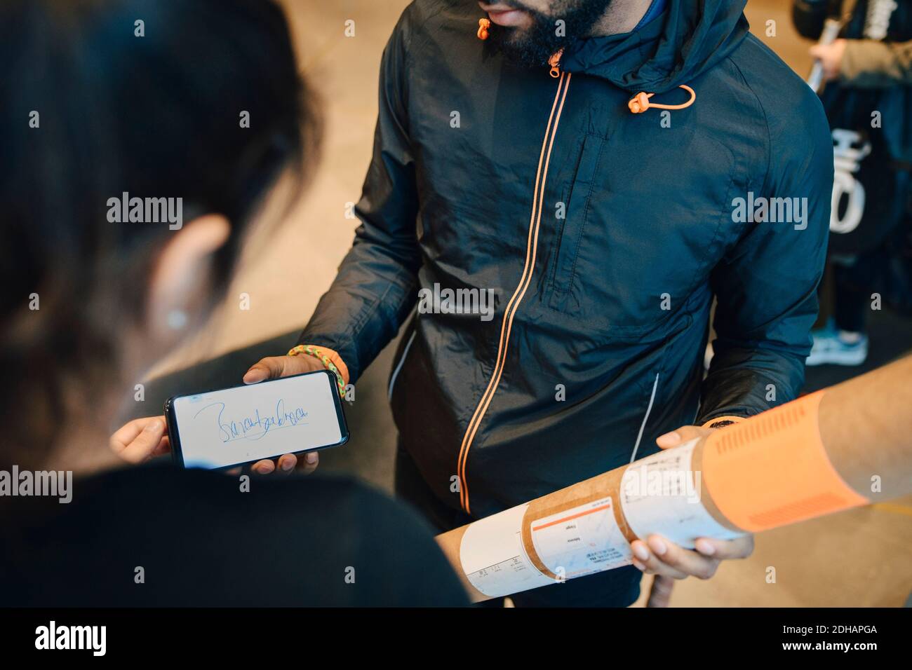 Mann hält das Paket, während er die Unterschrift des Kunden auf dem Handy betrachtet Telefon Stockfoto