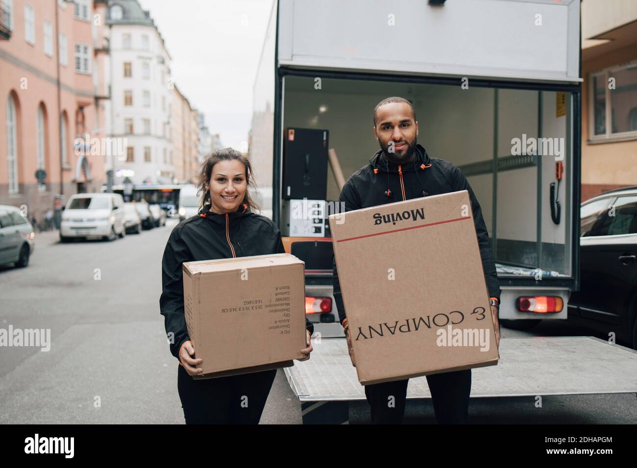 Portrait von männlichen und weiblichen Arbeitern, die im Stehen Kisten tragen Gegen Lieferwagen in der Stadt Stockfoto