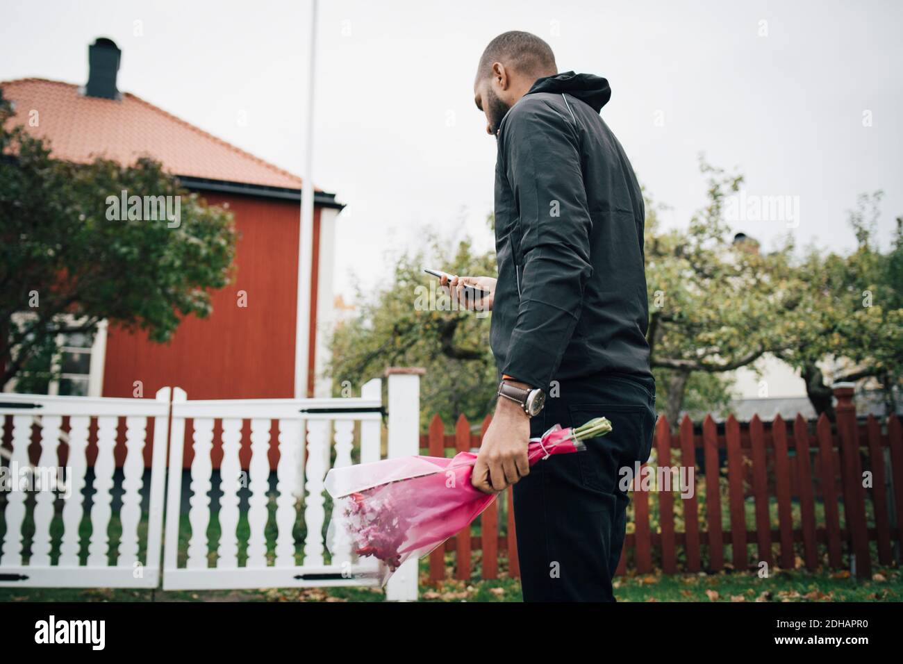 Mann, der Blumenstrauß hält, während er das Mobiltelefon benutzt Haus Stockfoto