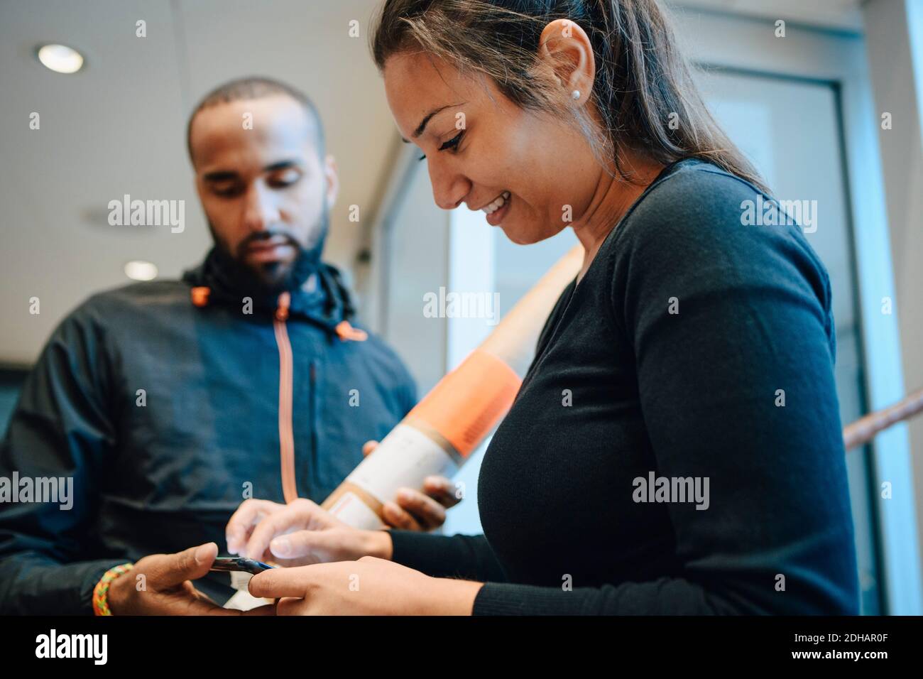 Lächelnde Frau, die auf dem Handy für ihre Lieferung von signiert Junger Bote Stockfoto