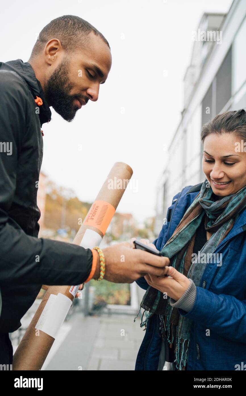Lächelnde Frau, die auf dem Handy für ihre Paketzustellung signiert Von einem männlichen Arbeiter Stockfoto