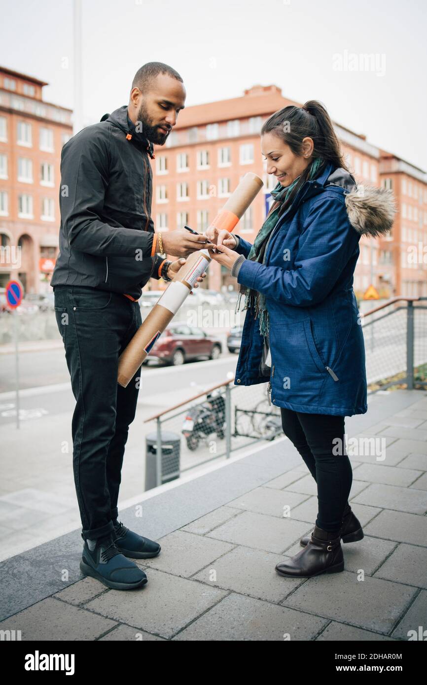Frau, die Smartphone für Unterschrift während der Lieferung von Messenger In der Stadt Stockfoto