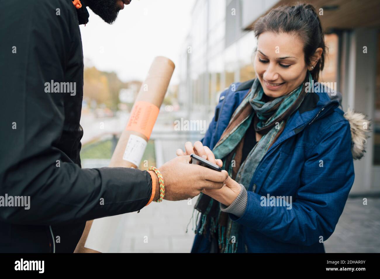Lächelnde Kundin, die auf dem Mobiltelefon für ihre Lieferung von signiert Männlicher Arbeiter Stockfoto