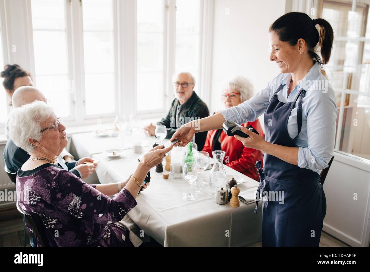 Glücklicher Besitzer, der einem älteren Erwachsenen während des Sitzens eine Kreditkarte gab Am Tisch mit Freunden Stockfoto