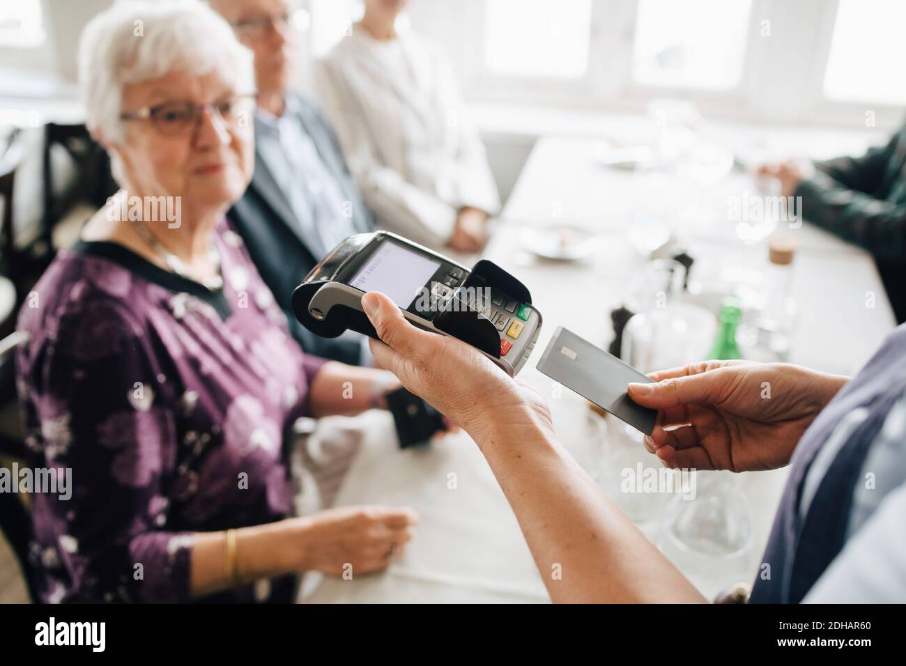 Mittelteil des Besitzers schieben Kreditkarte während Senior Mann und Frauen sitzen am Tisch im Restaurant Stockfoto