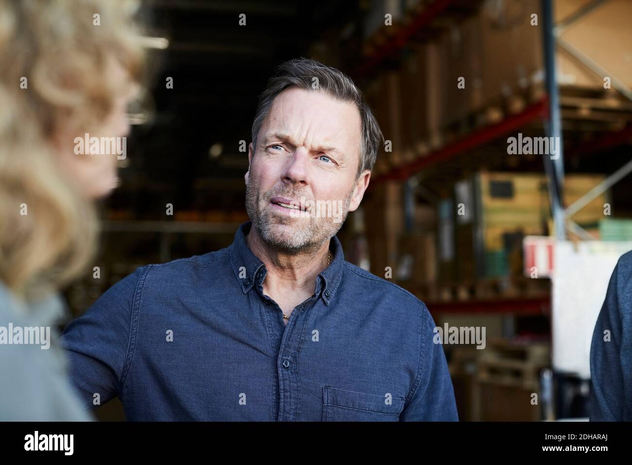 Reifer männlicher Arbeiter, der eine Kollegin im Lager ansieht Stockfoto