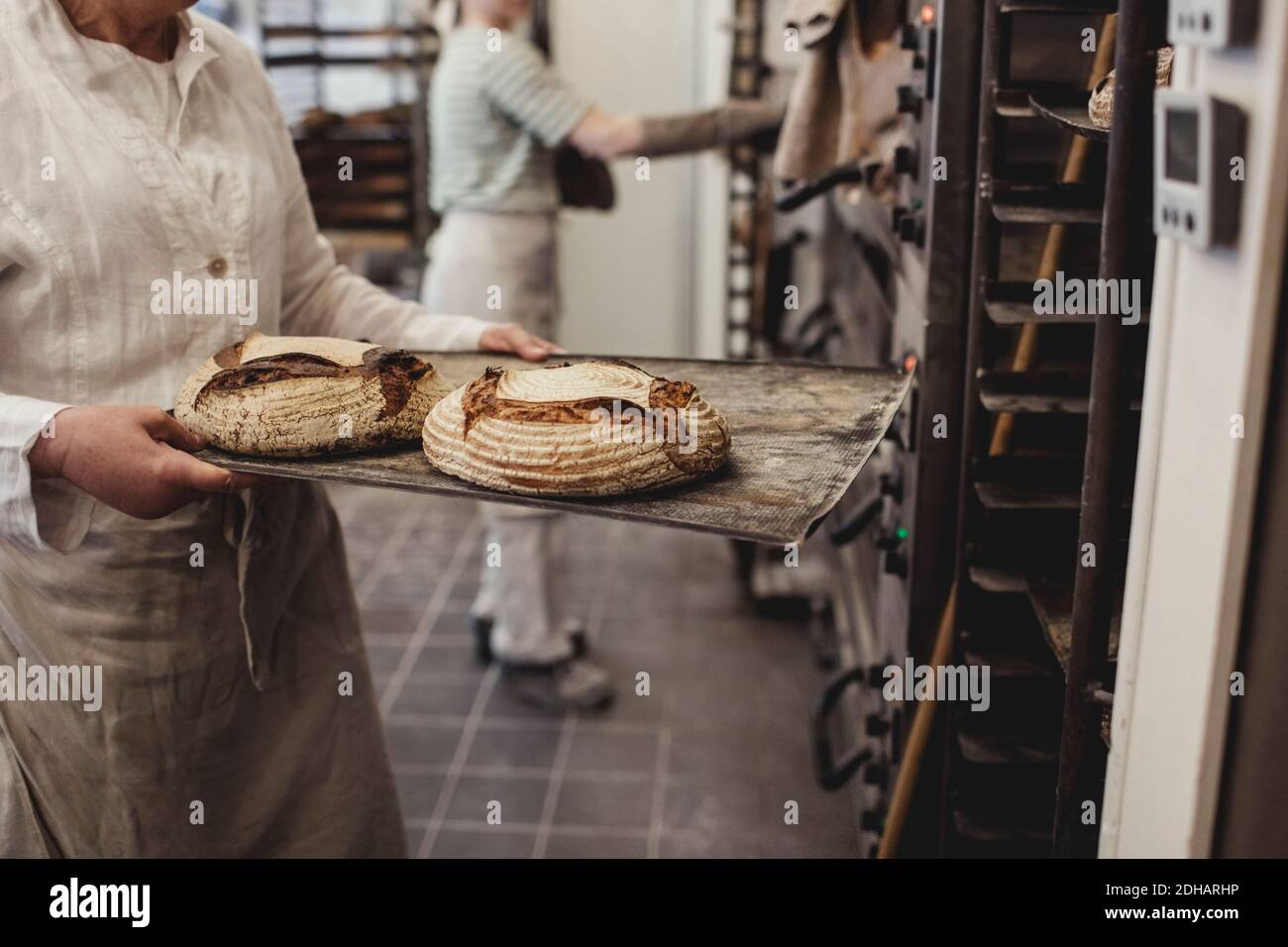 Mittelteil des Bäckers hält frisch gebackenes Brot auf Kühlregal In der Bäckerei Stockfoto
