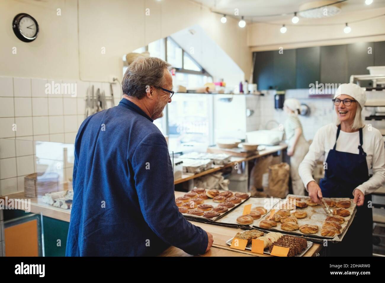 Lächelnde Besitzerin, die dem Gast frisch gebackenes Essen zeigt Bäckerei Stockfoto