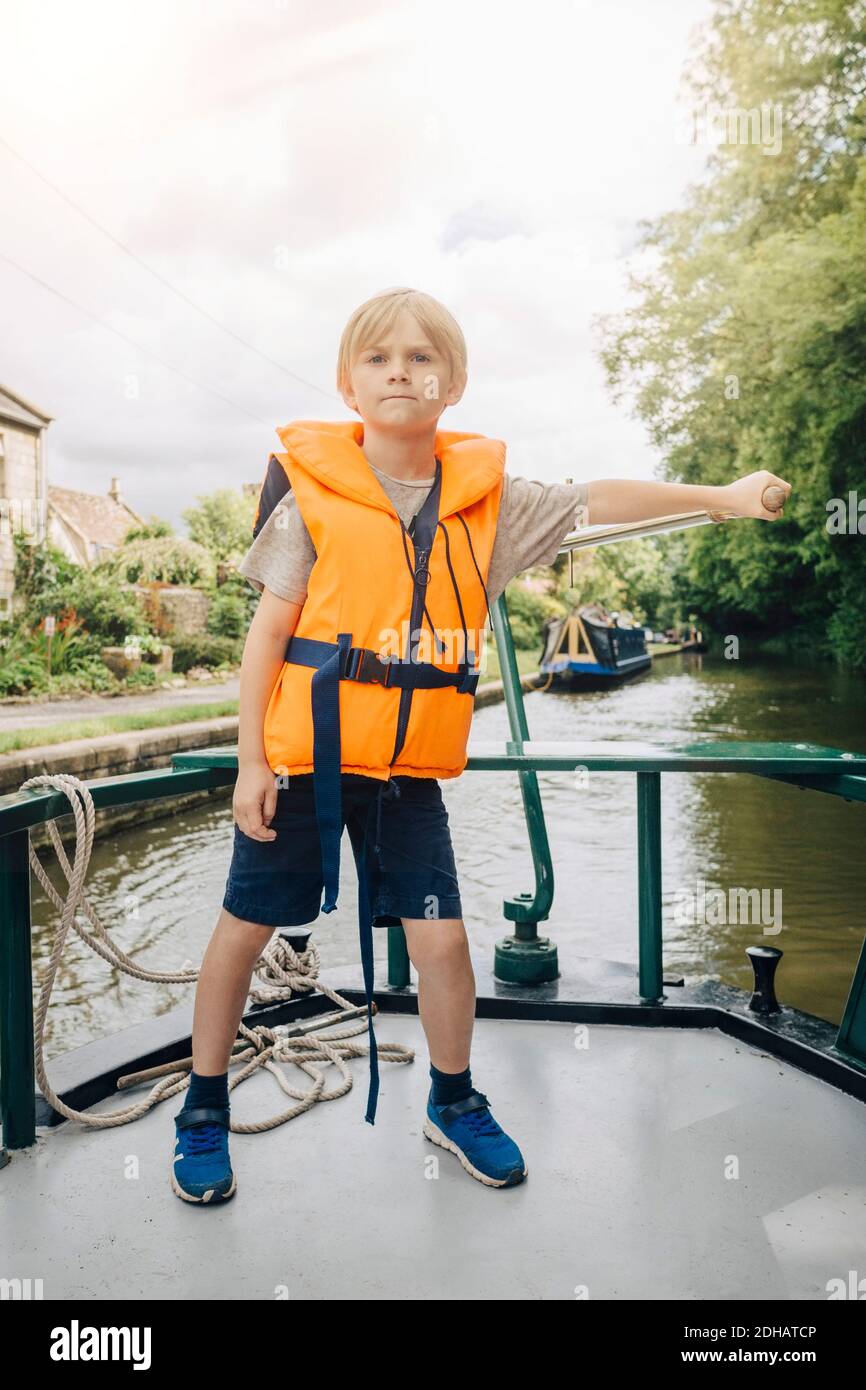 Volle Länge des selbstbewussten Jungen Steuerboot im Fluss gegen Himmel Stockfoto