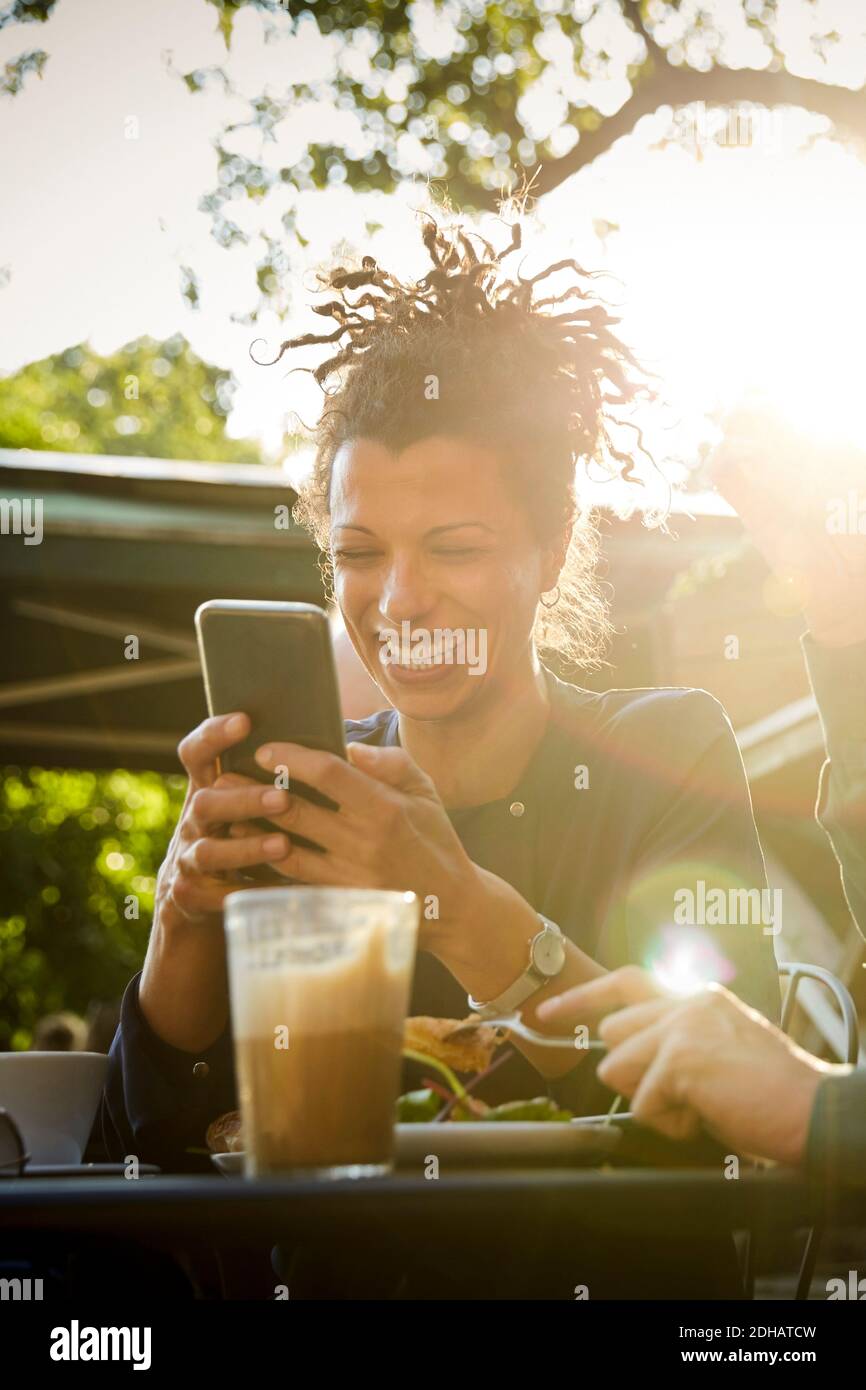 Lächelnde Architektin mit Mobiltelefon beim Mittagessen Mitarbeiter im Café im Freien an sonnigen Tagen Stockfoto