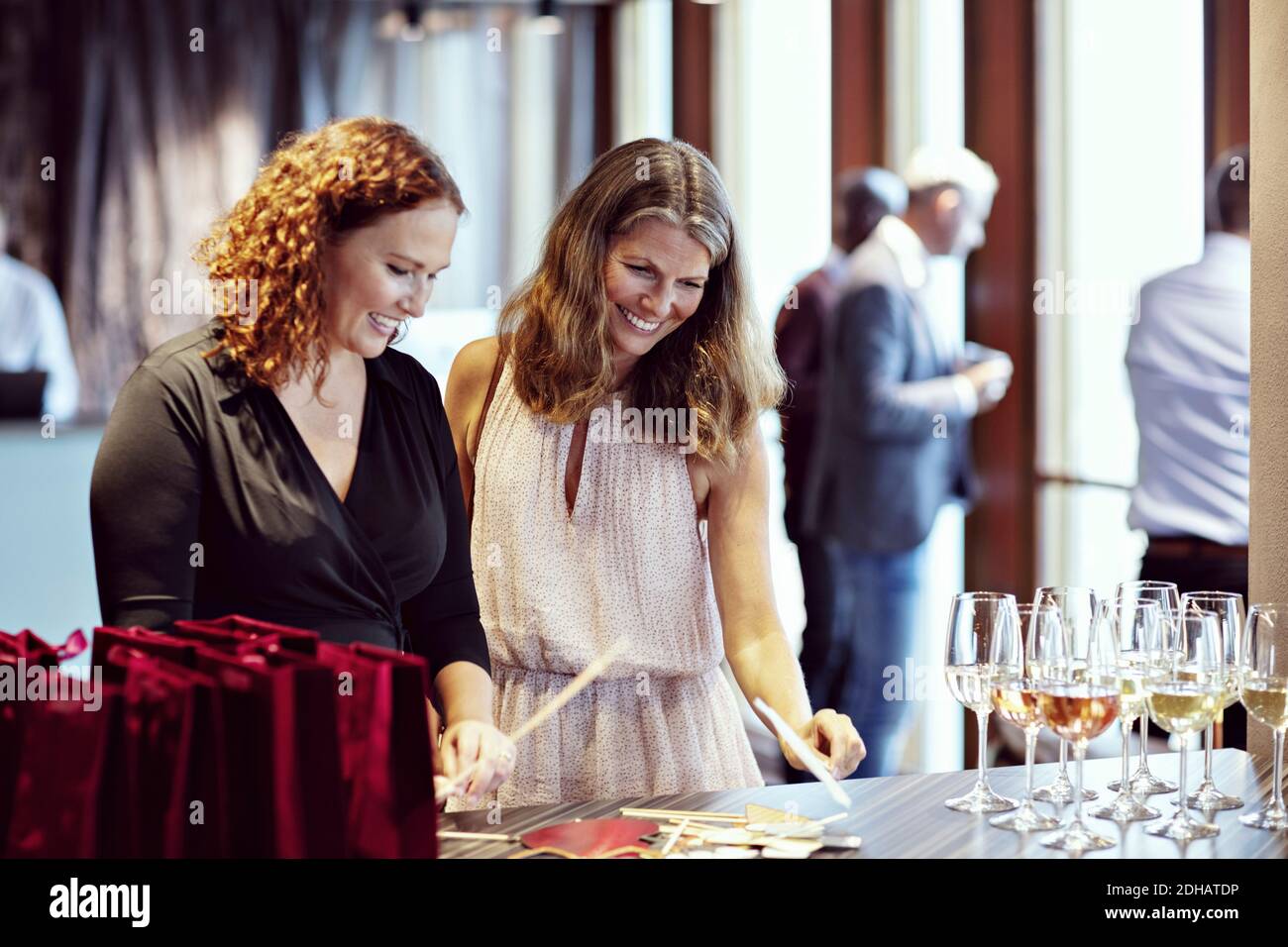 Lächelnde Geschäftsfrauen, die Requisiten von Weinläsern auf dem Tisch betrachten Büroparty Stockfoto