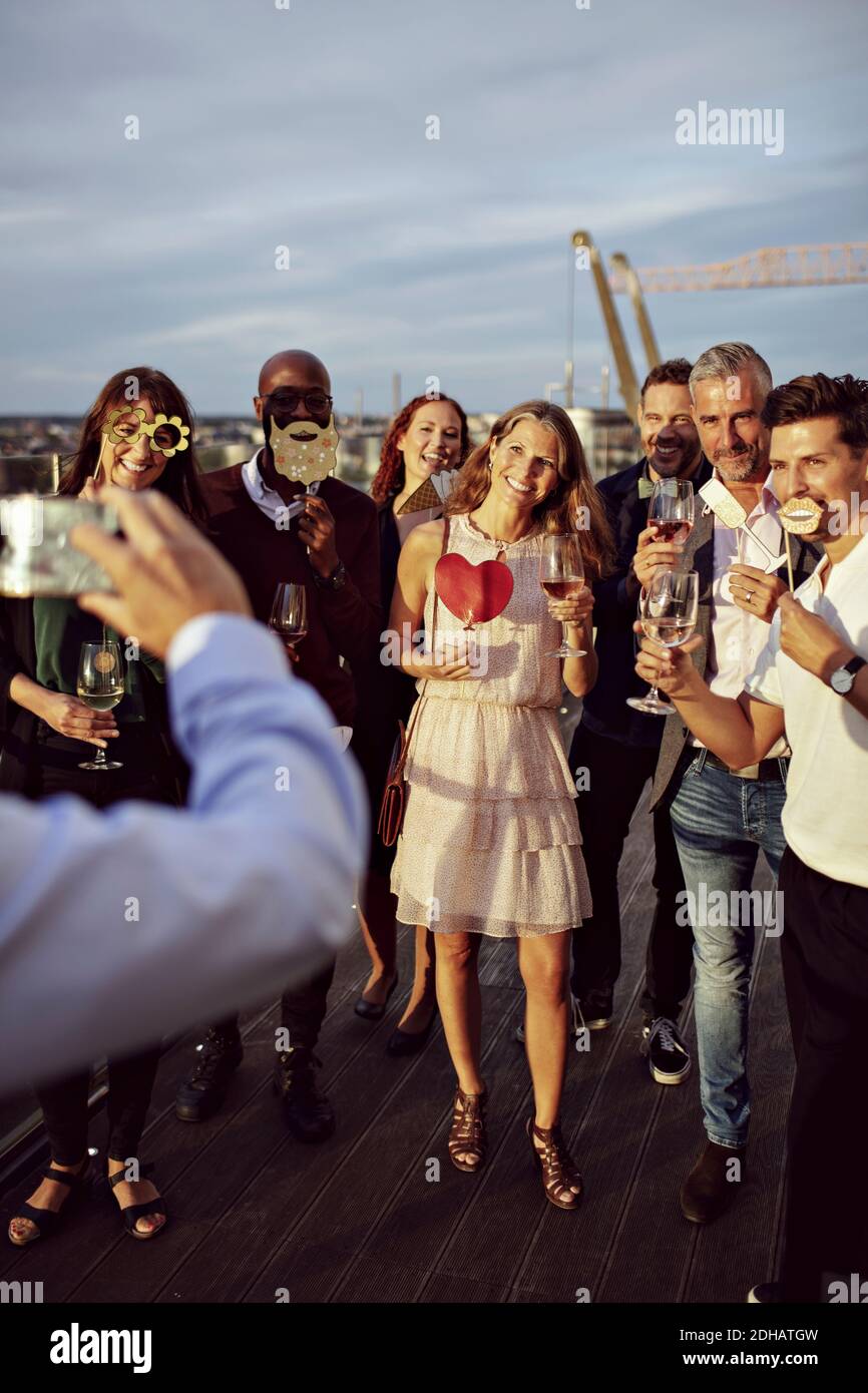 Geschäftsmann fotografiert glückliche Mitarbeiter, die Weingläser und Requisiten im Büro halten Terrasse in Party Stockfoto