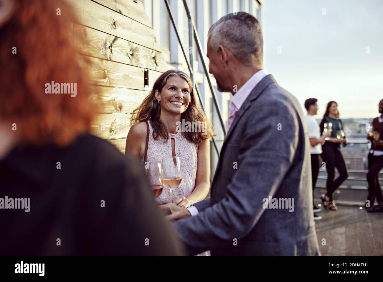 Lächelnde Geschäftsfrau im Gespräch mit Kollegen in Partei auf der Terrasse Stockfoto