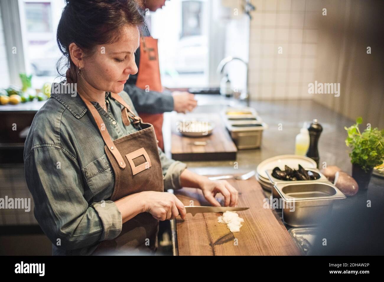 Reife weibliche Köchin schneidet Essen an Bord an der Theke in Restaurant Küche Stockfoto