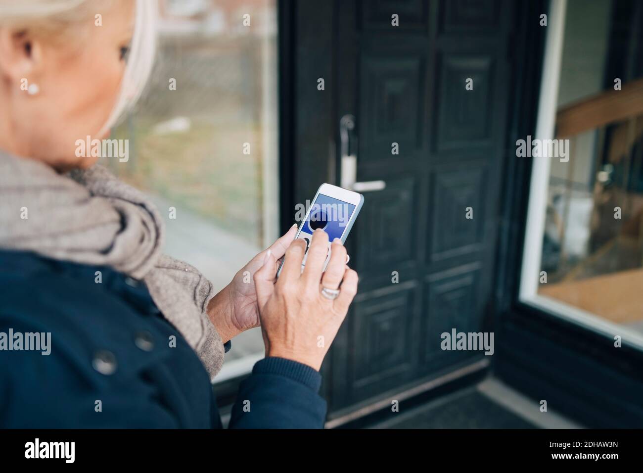 High-Winkel-Ansicht der Frau entriegelt Haustür durch smart Telefon-App Stockfoto