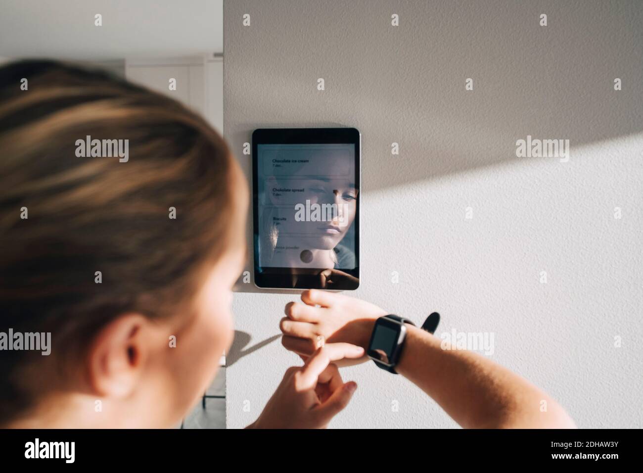 Teenage-Mädchen Anpassung Smart-Uhr mit digitalen Tablet montiert auf Weiße Wand zu Hause Stockfoto