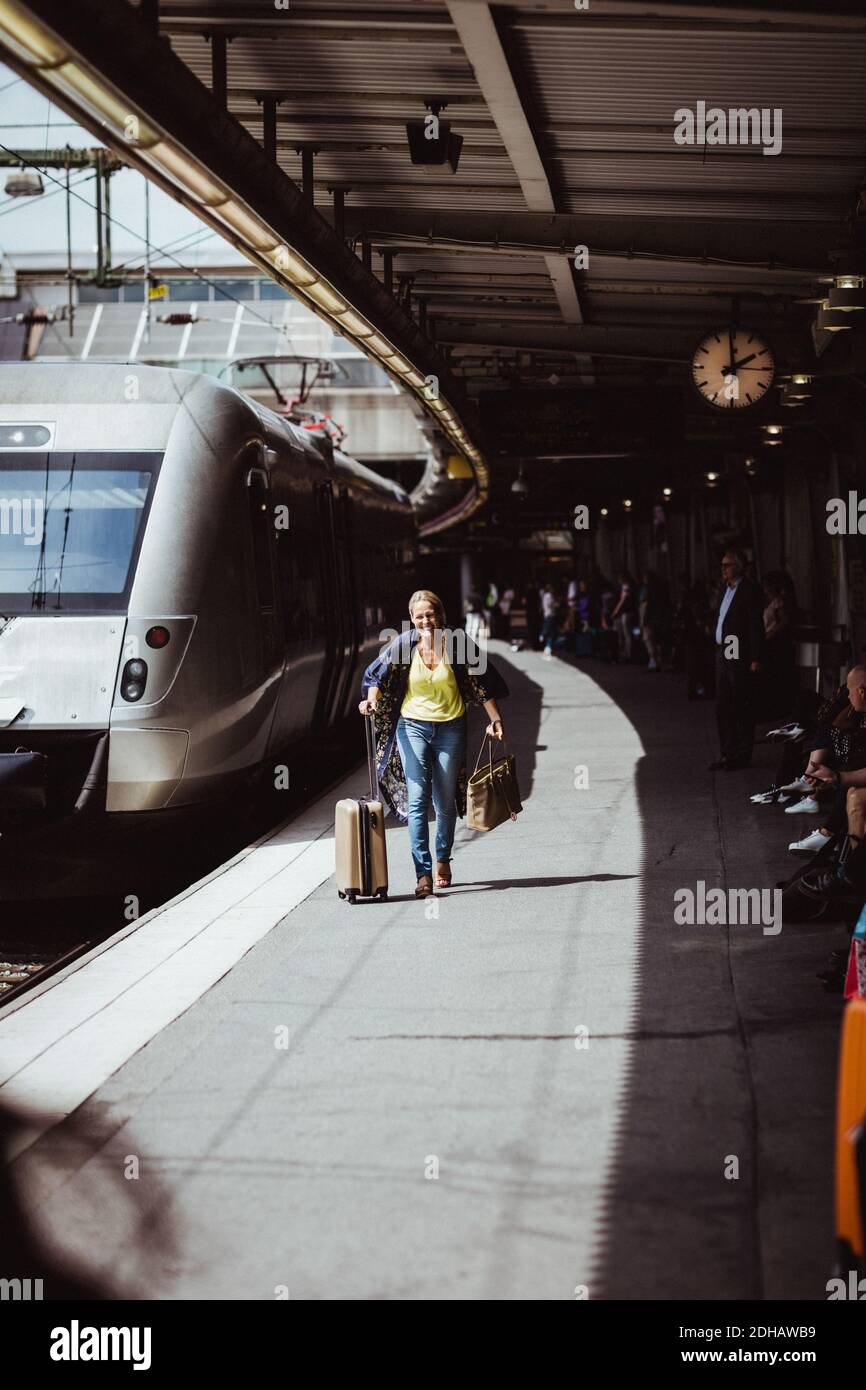 Volle Länge der glücklichen Frau mit Gepäck läuft auf der Eisenbahn Bahnsteig Stockfoto