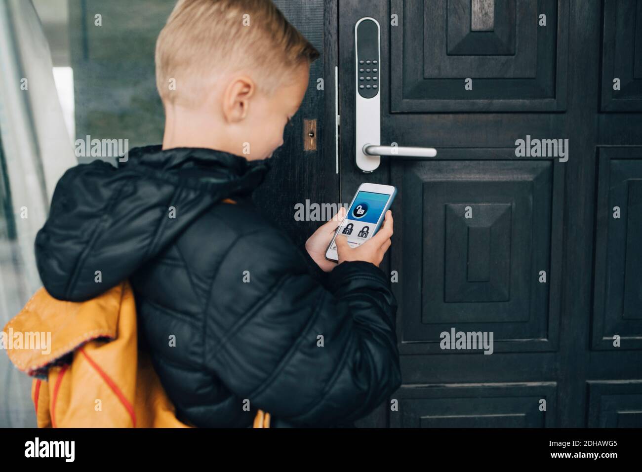 Rückansicht des Jungen mit App auf Smartphone zu Haustür entriegeln Stockfoto