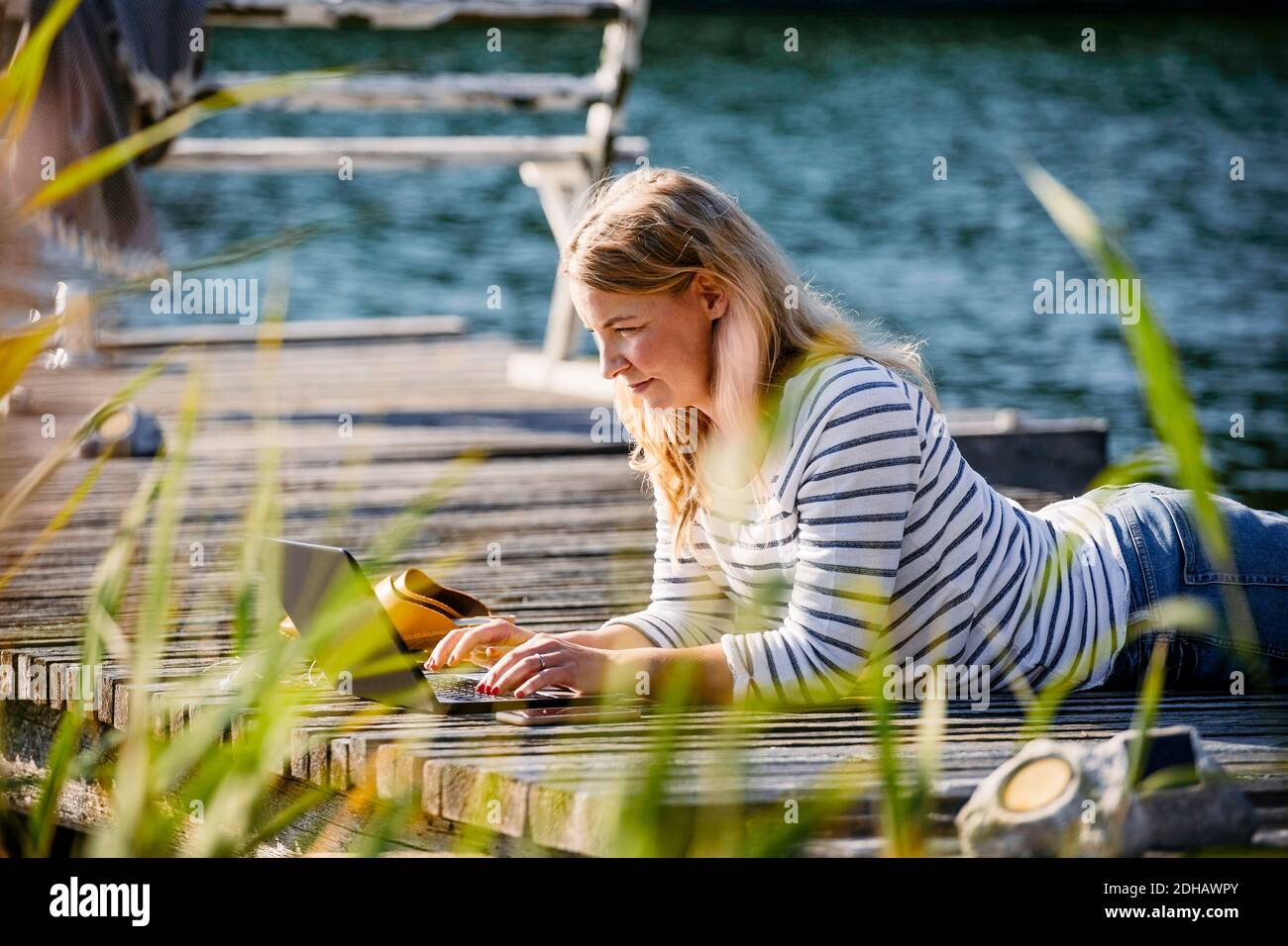 Frau, die auf der Vorderseite lag, während sie am Pier über einem Laptop arbeitete Im Sommer Stockfoto