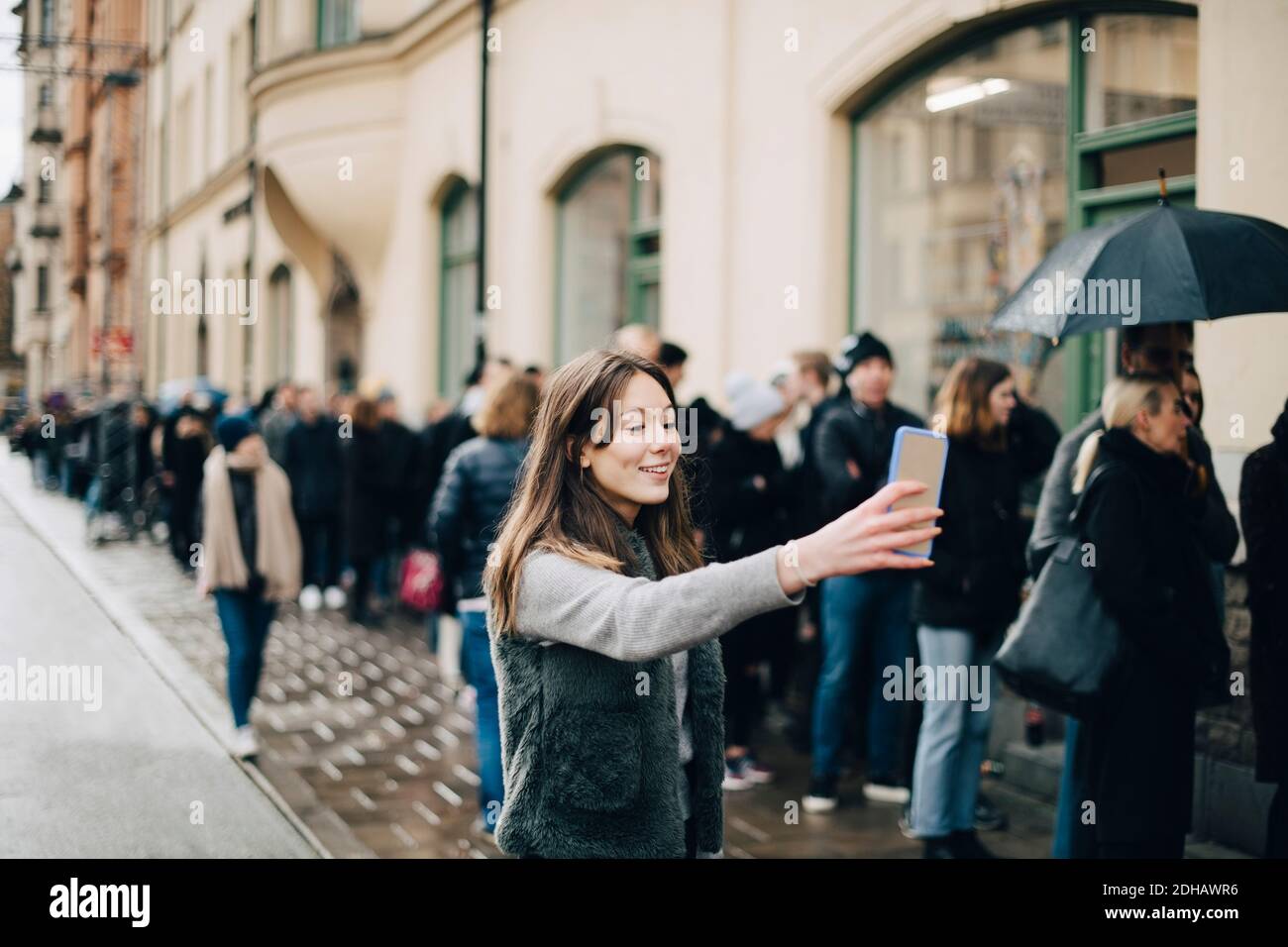 Lächelndes Mädchen nimmt Selfie durch Smartphone gegen die Menge in Stadt Stockfoto