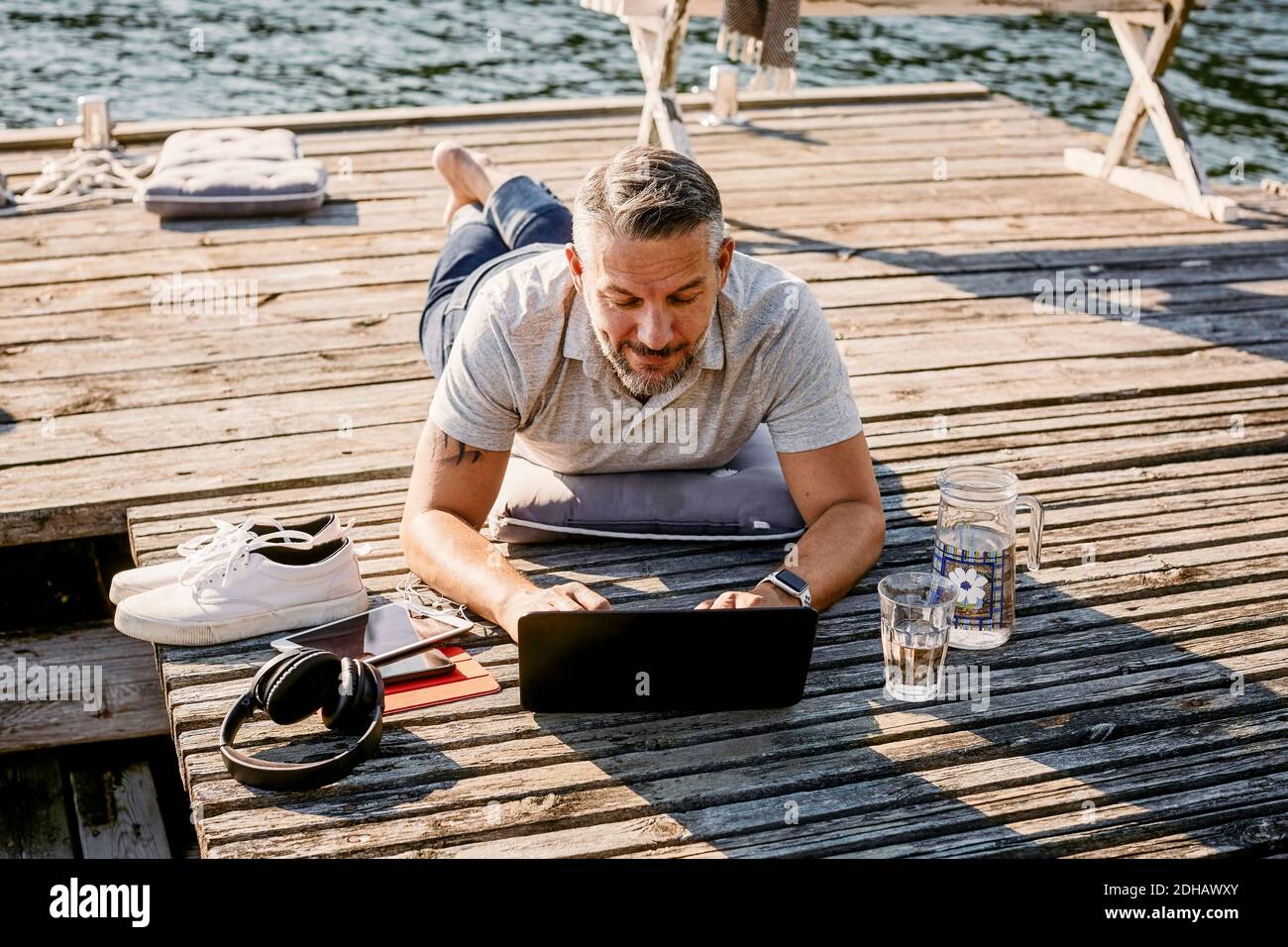 Reifer Mann liegt auf der Vorderseite, während mit Laptop über Holz Steg Stockfoto