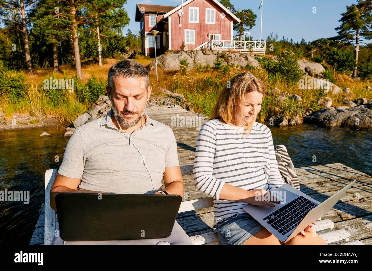 Paar mit Laptop, während auf der Bank zusammen am Pier sitzen Im Sommer Stockfoto