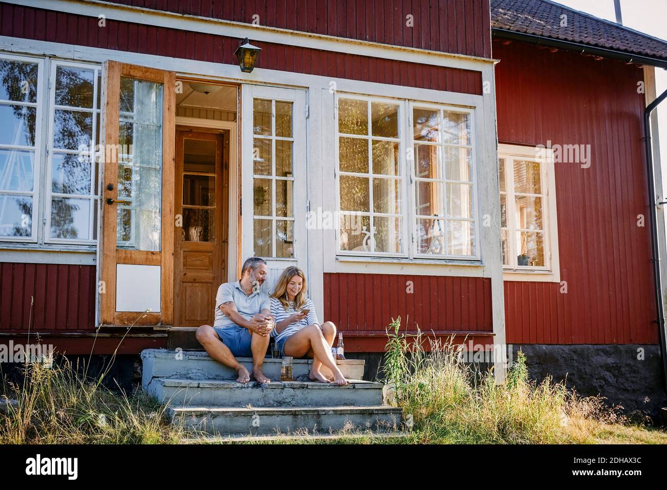 Ein Paar schaut auf das Smartphone, während es draußen auf einer Treppe sitzt Blockhütte Stockfoto