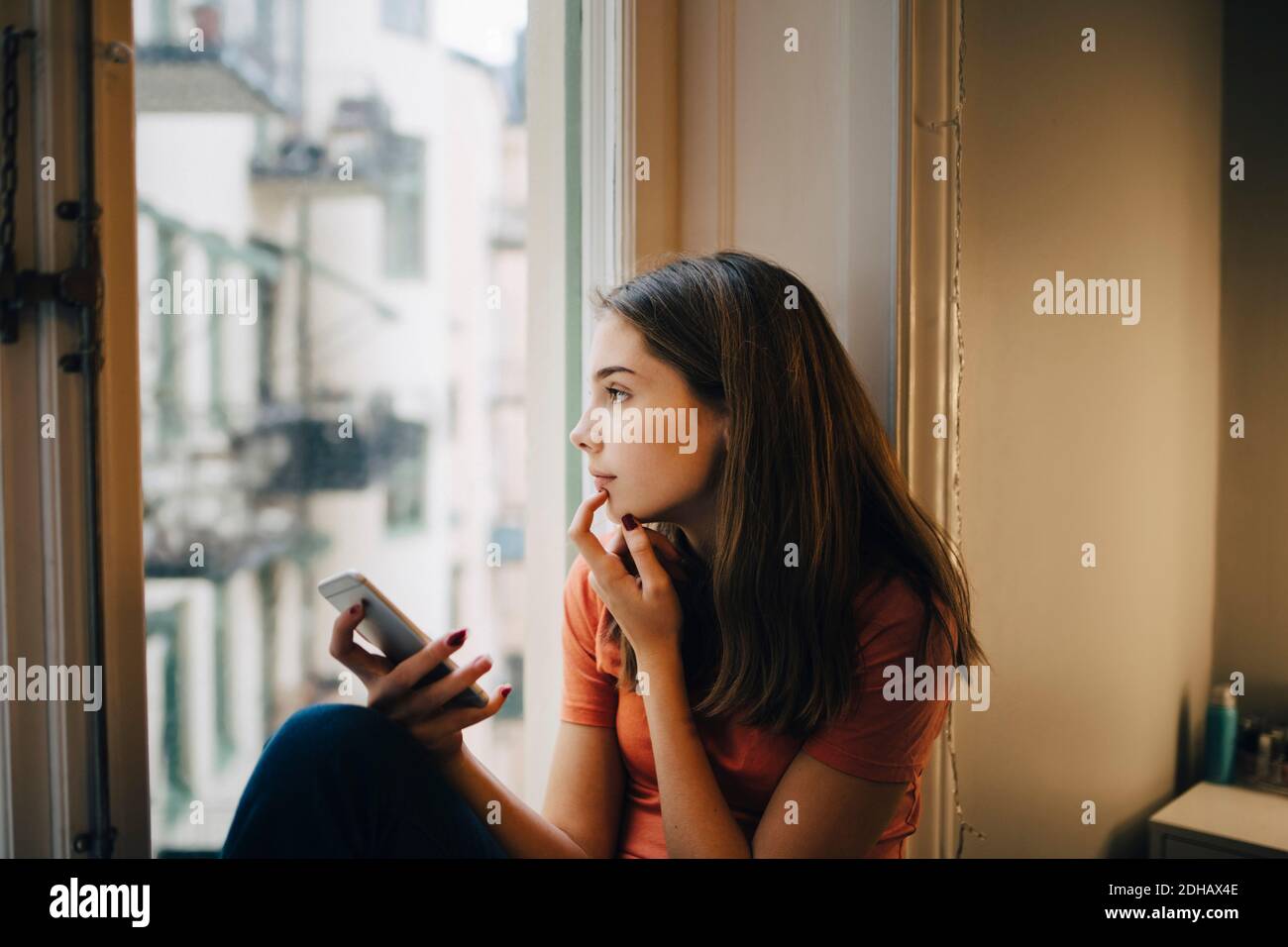 Nachdenklich Mädchen mit Telefon, während sitzen am Fenster Schweller Stockfoto