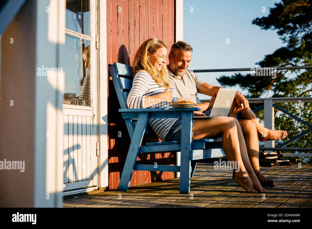 Lächelndes Paar mit Laptop beim Frühstück auf der Veranda Blockhütte Stockfoto