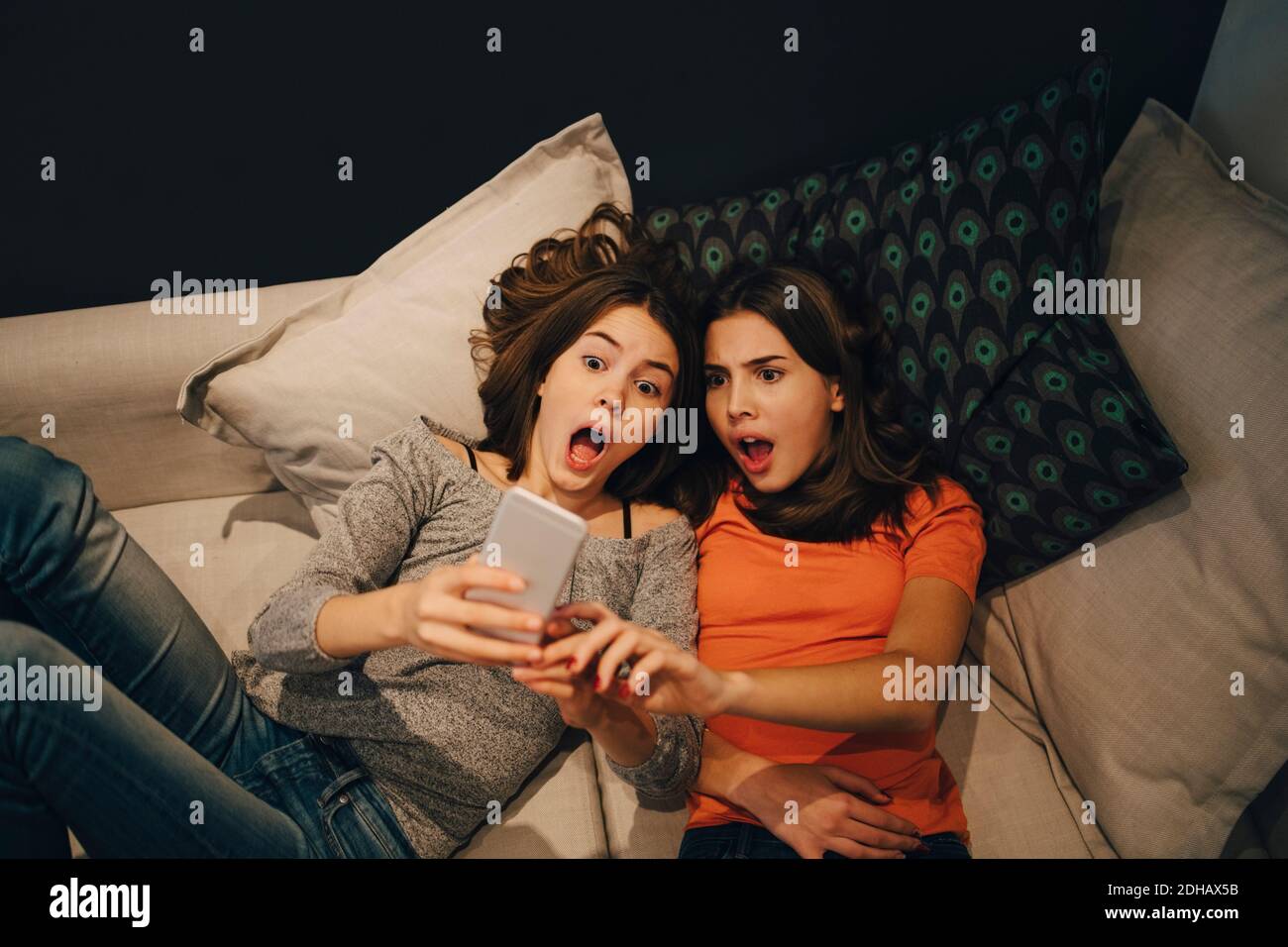 High-Angle-Ansicht von Freunden mit offenem Mund über Telefon Während Sie sich zu Hause auf dem Sofa ausruhen Stockfoto