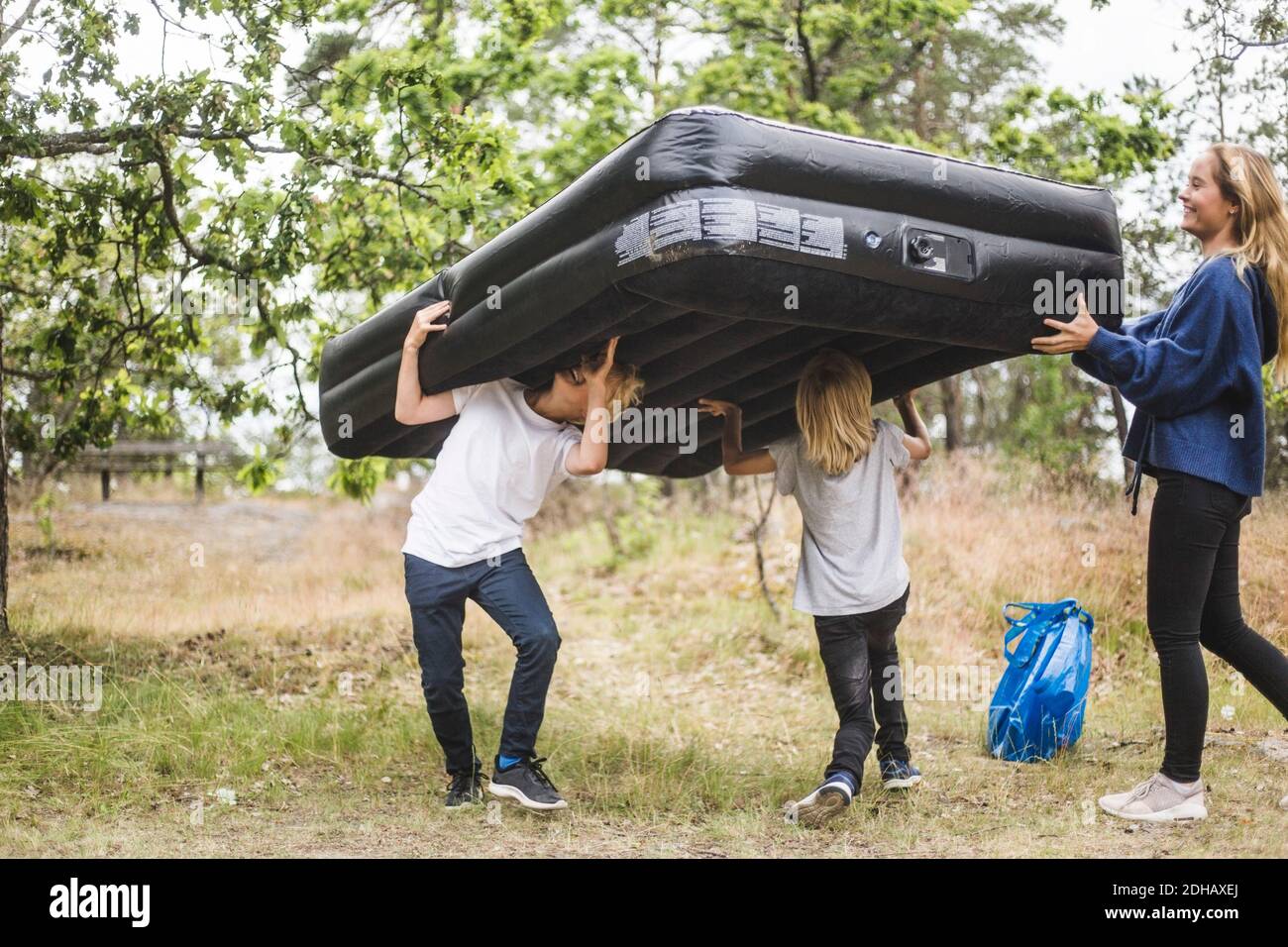 Volle Länge der Teenager-Mädchen mit Spaß mit Geschwistern, während Aufblasbare Matratze zusammen auf dem Campingplatz tragen Stockfoto