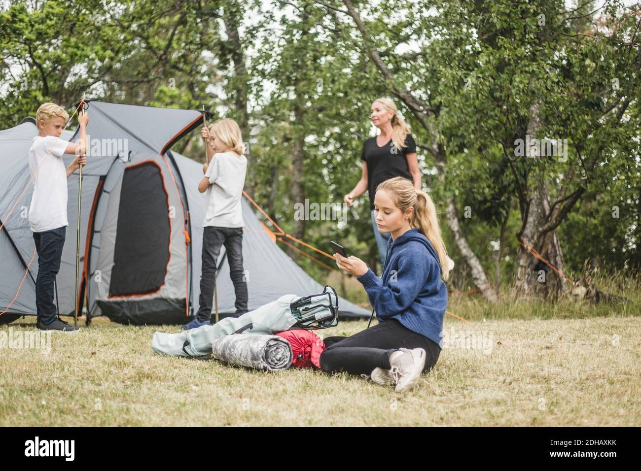 Teenager SMS auf Handy, während die Familie Zelt Pitching Stockfoto