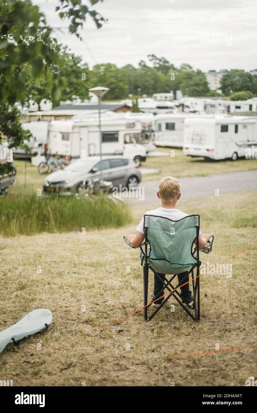 Rückansicht des Jungen, der auf Campingstuhl sitzt, während er schaut Bei Reiseanhängern Stockfoto