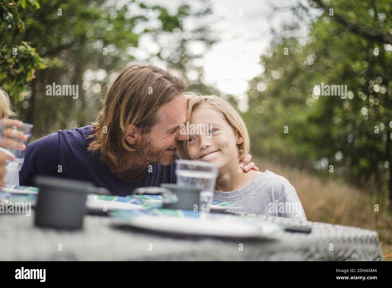 Liebevoller Vater umarmt Tochter am Tisch auf dem Campingplatz Stockfoto