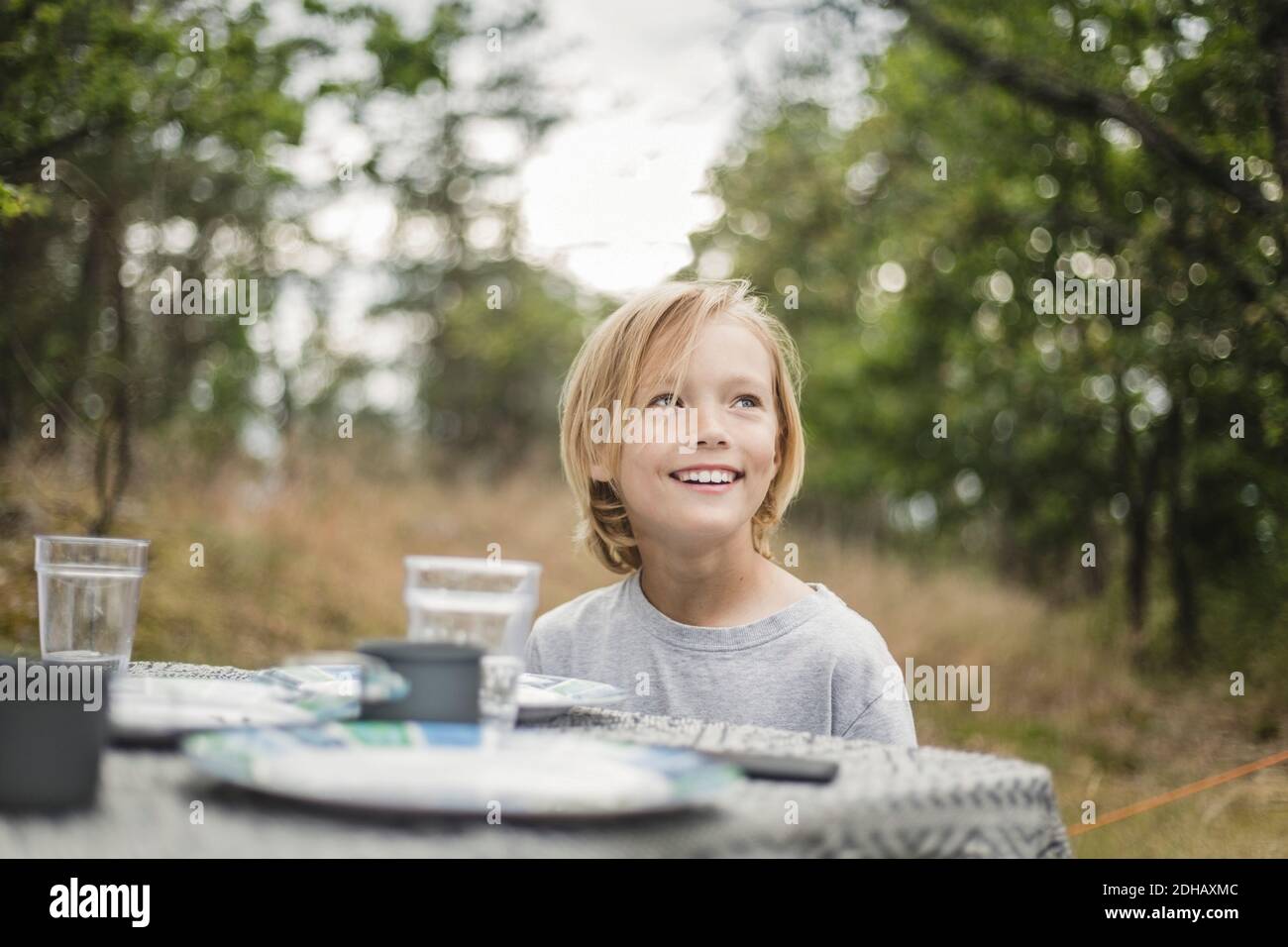 Lächelndes Mädchen, das wegschaut, während es am Tisch im Wald sitzt Stockfoto