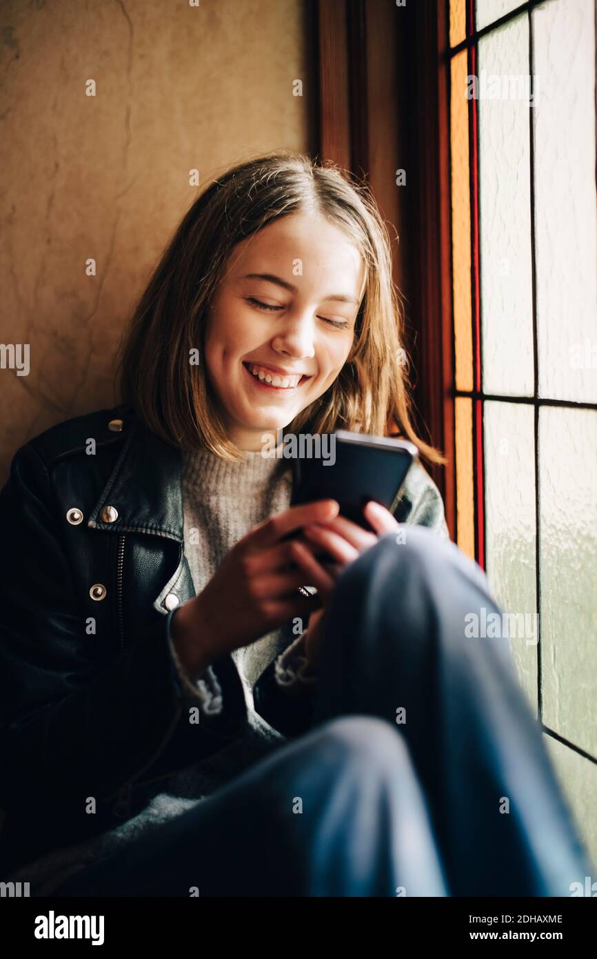 Glückliches Mädchen mit Smartphone, während sitzen am Fenster an Zu Hause Stockfoto