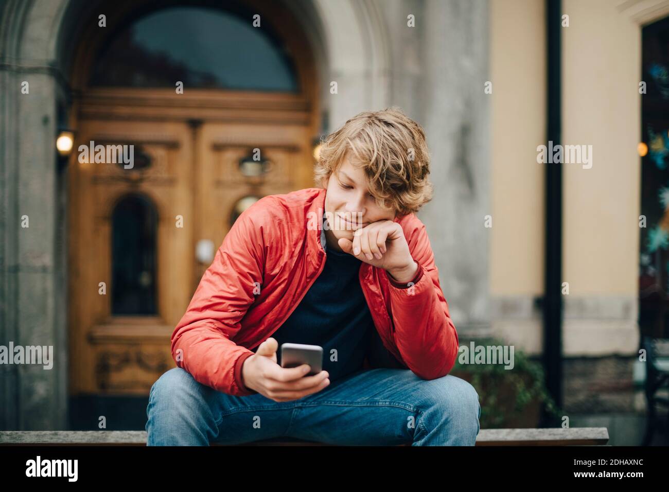 Teenager-Junge mit Handy, während auf der Bank sitzen in Stadt Stockfoto