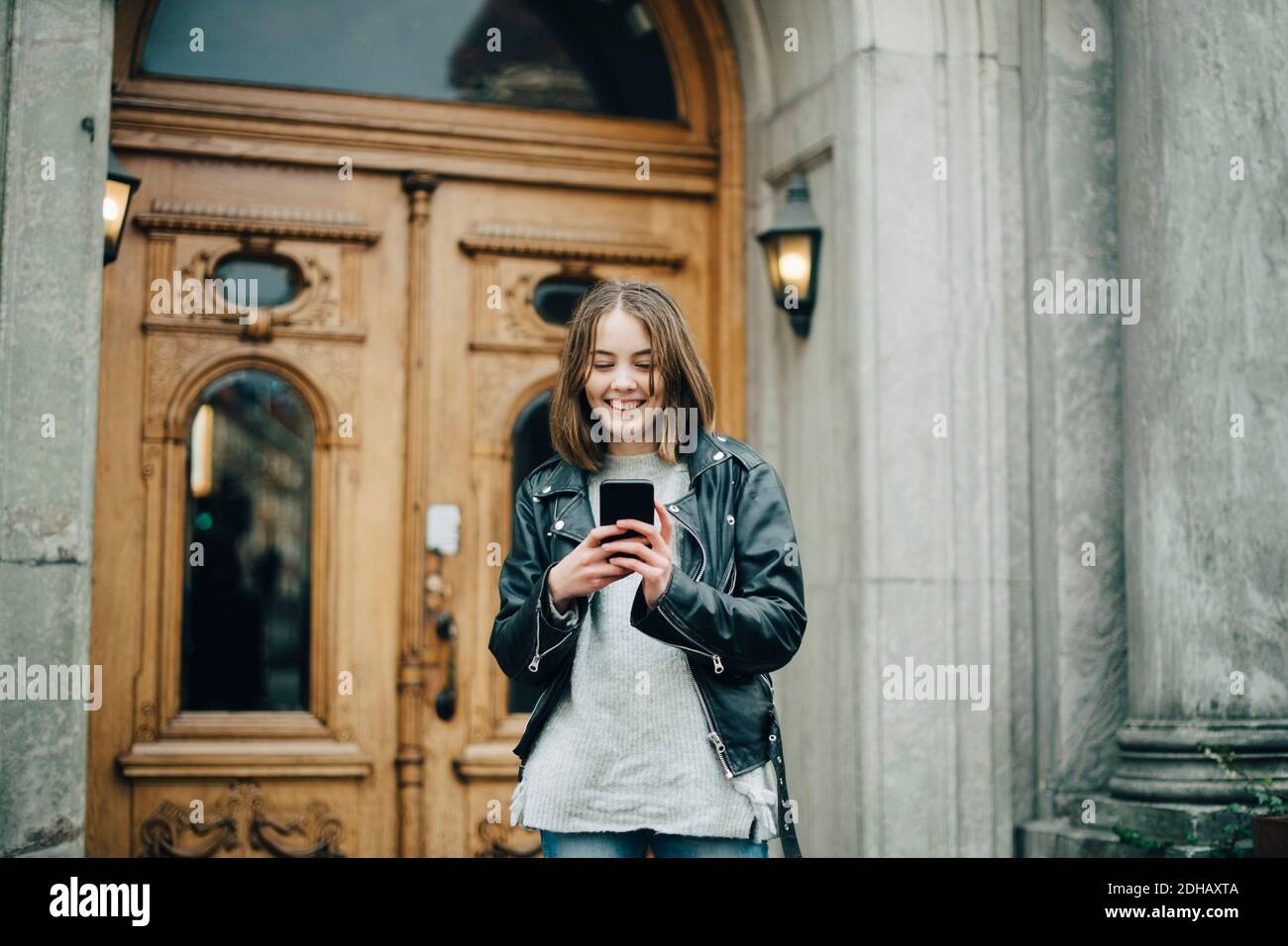 Lächelndes Mädchen mit Handy, während sie gegen Gebäude stehen Stockfoto