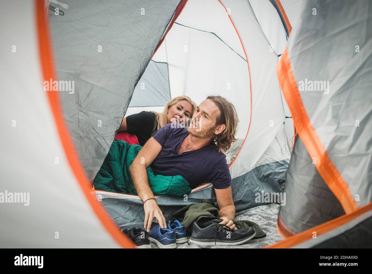 Ein Paar guckt durch das Zelt, während es sich im Schlafsack lehnt Camping Stockfoto
