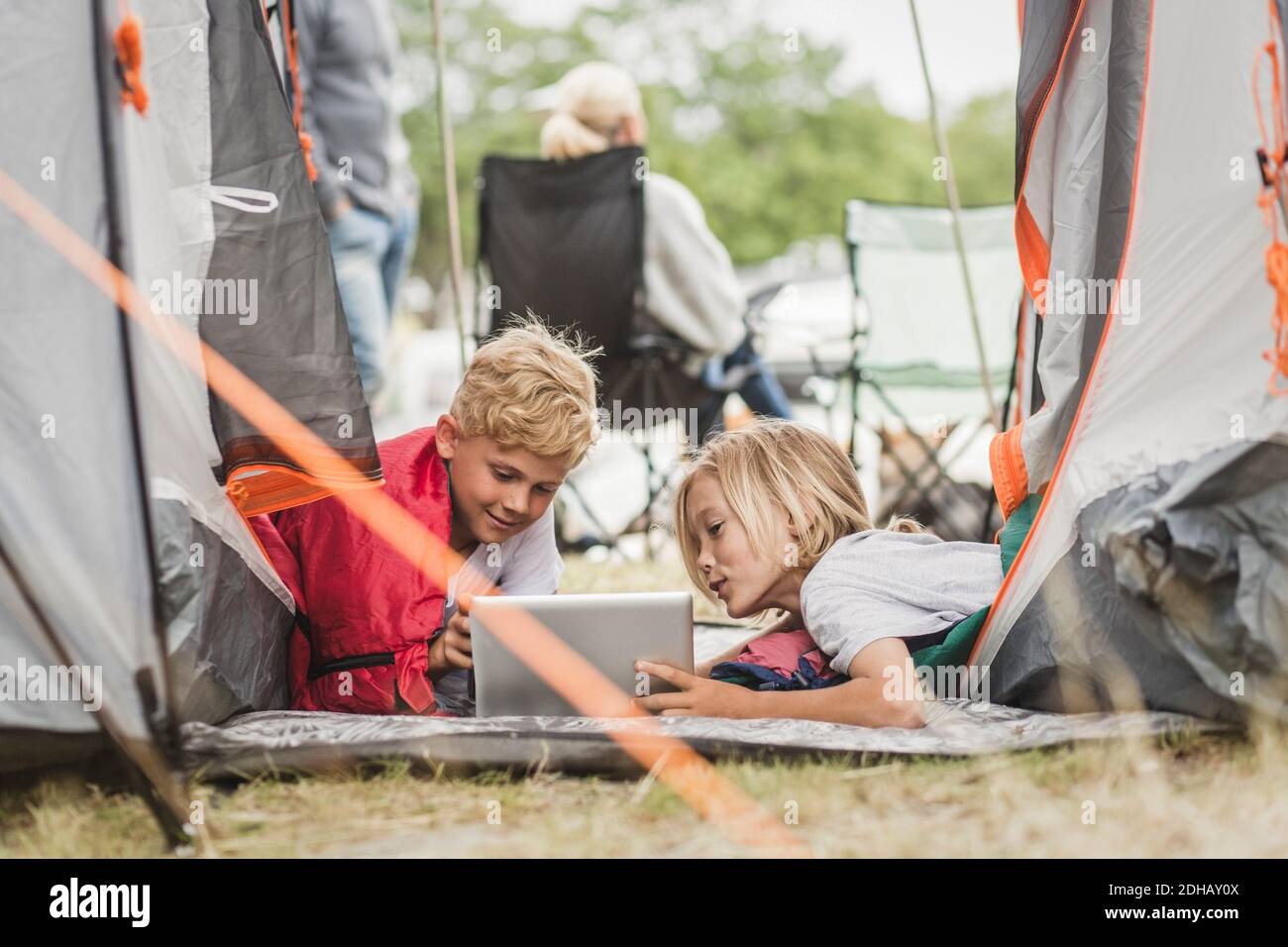 Geschwister sprechen während der Nutzung von digitalen Tablet im Zelt auf dem Campingplatz Stockfoto