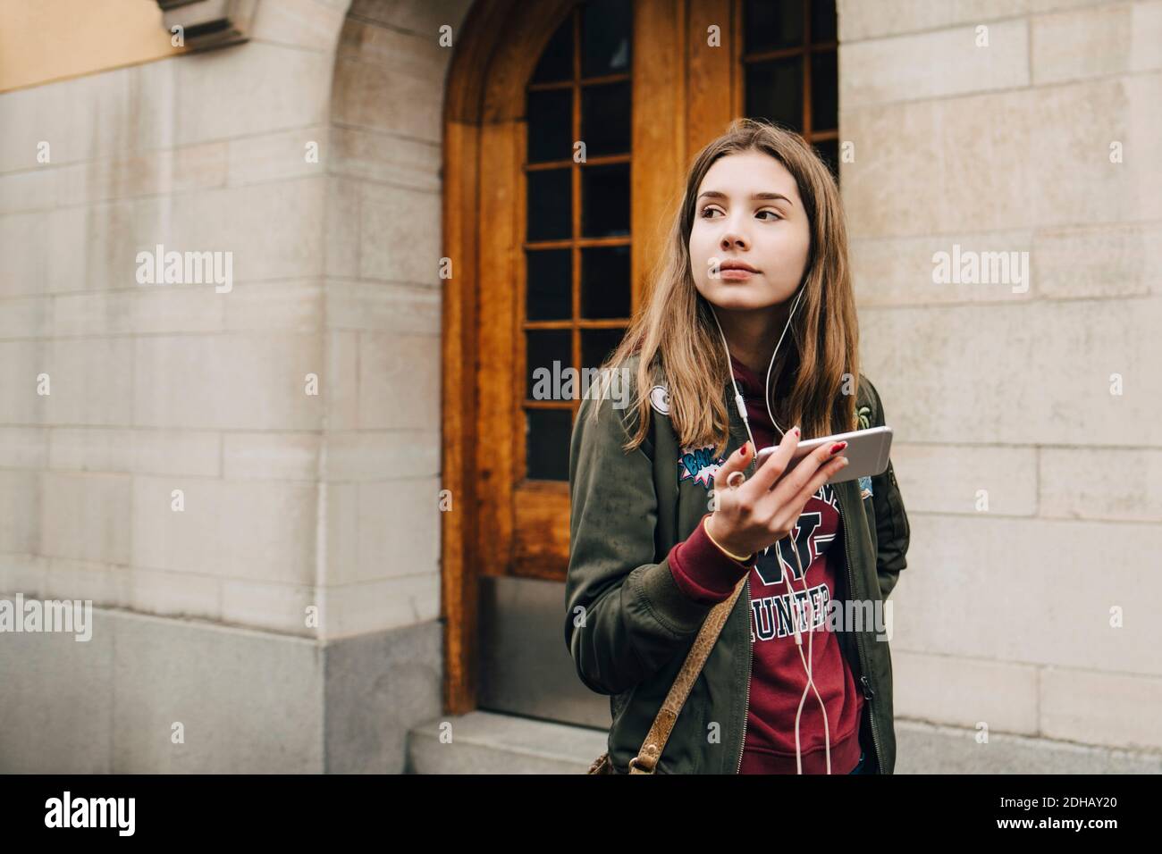 Nachdenklich Mädchen Musik hören über Smartphone, während zu Fuß vorbei Wand Stockfoto