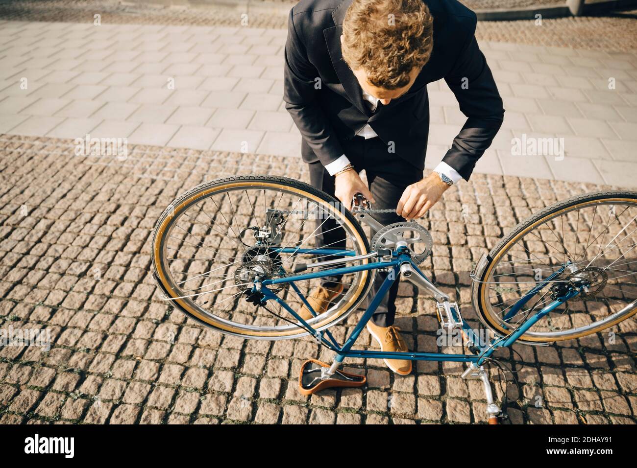 Blick in den hohen Winkel des Geschäftsmannes, der die Fahrradkette auf Kopfsteinpflaster repariert Fußweg in der Stadt Stockfoto