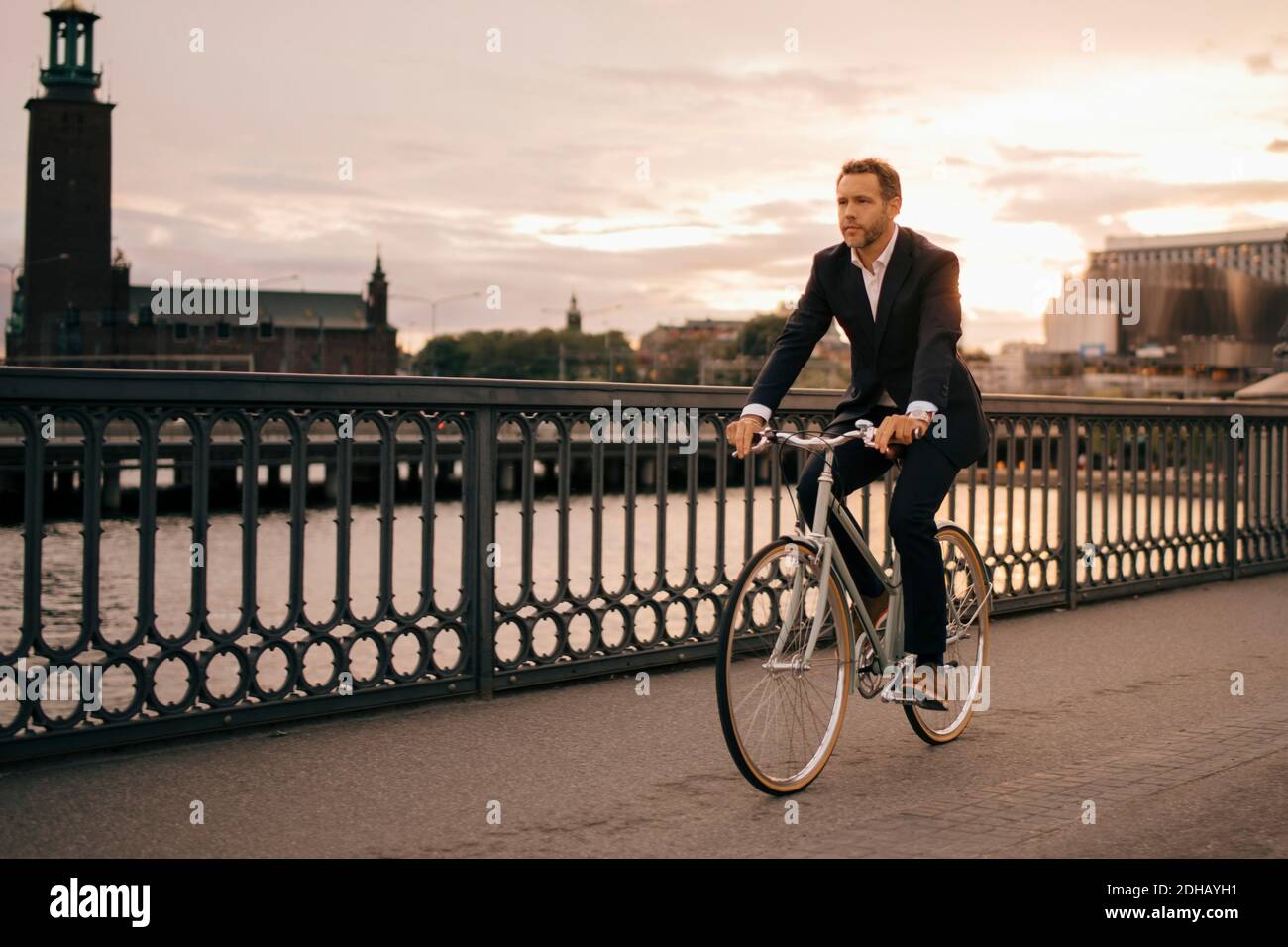 Volle Länge des Geschäftsmannes Radfahren auf Brücke in der Stadt während Sonnenuntergang Stockfoto