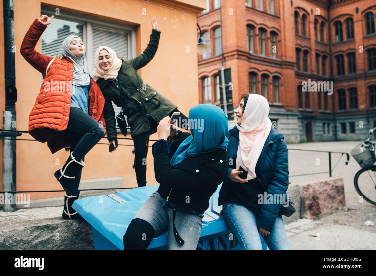 Junge Frau fotografiert fröhliche Freundinnen gegen Gebäude in der Stadt Stockfoto