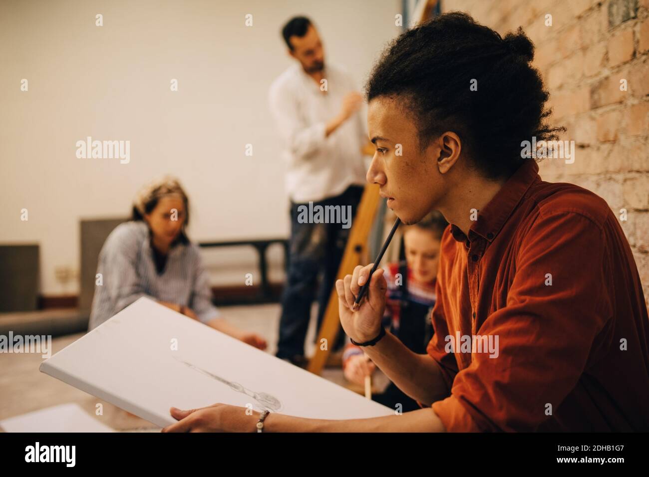 Nachdenkliche junge Künstler Malerei auf Leinwand mit Freunden im Hintergrund Stockfoto